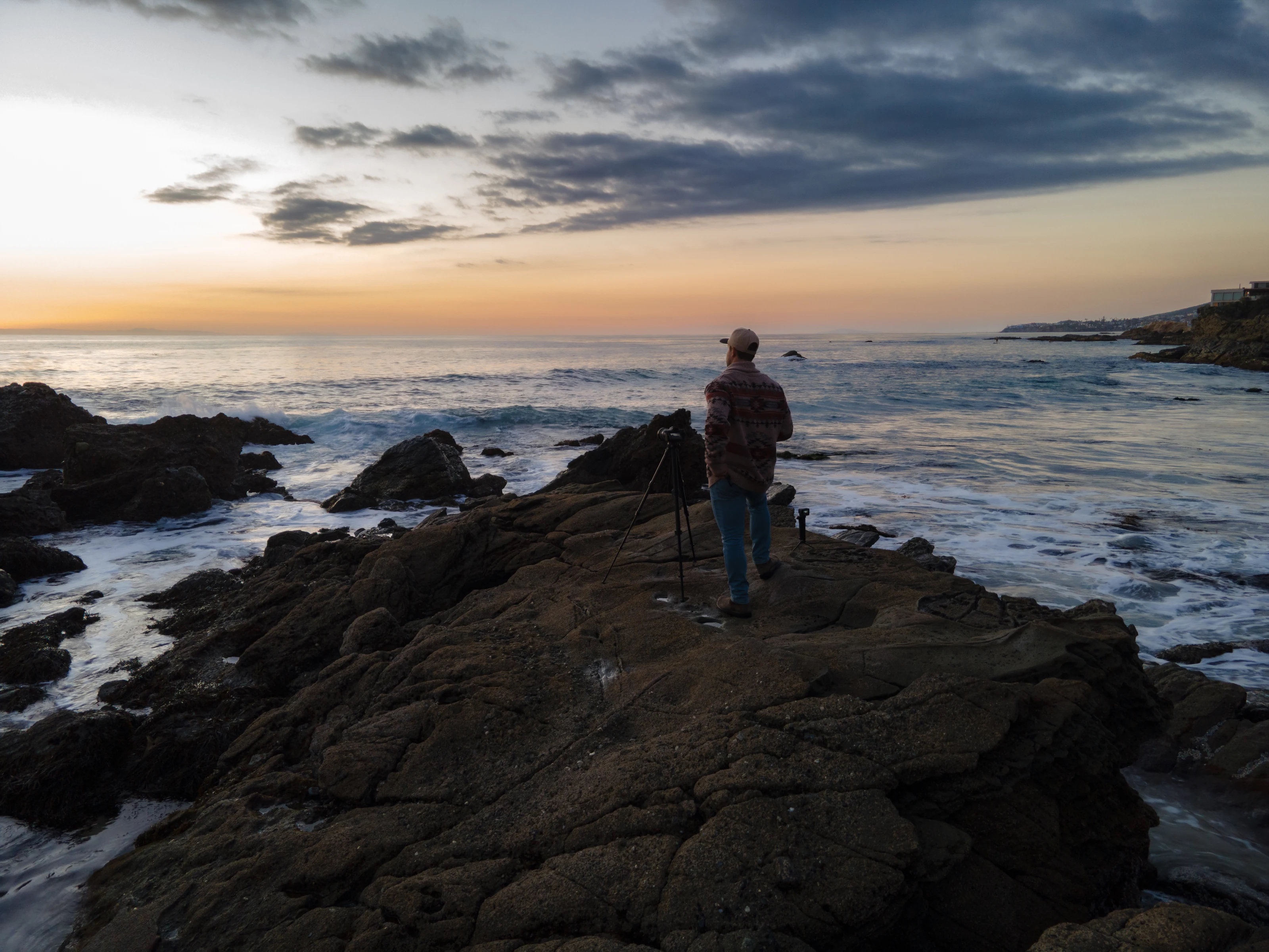 The founder standing with his tripod on coastal rocks at dusk